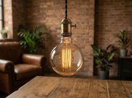 Ampoule globe G125 Gordon allumée, suspendue à une douille en laiton au-dessus d'une table en bois, mur de briques