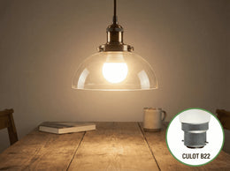 Ampoule LED sphérique G45 allumée dans une suspension en verre au-dessus d'une table en bois, encart sur le culot B22