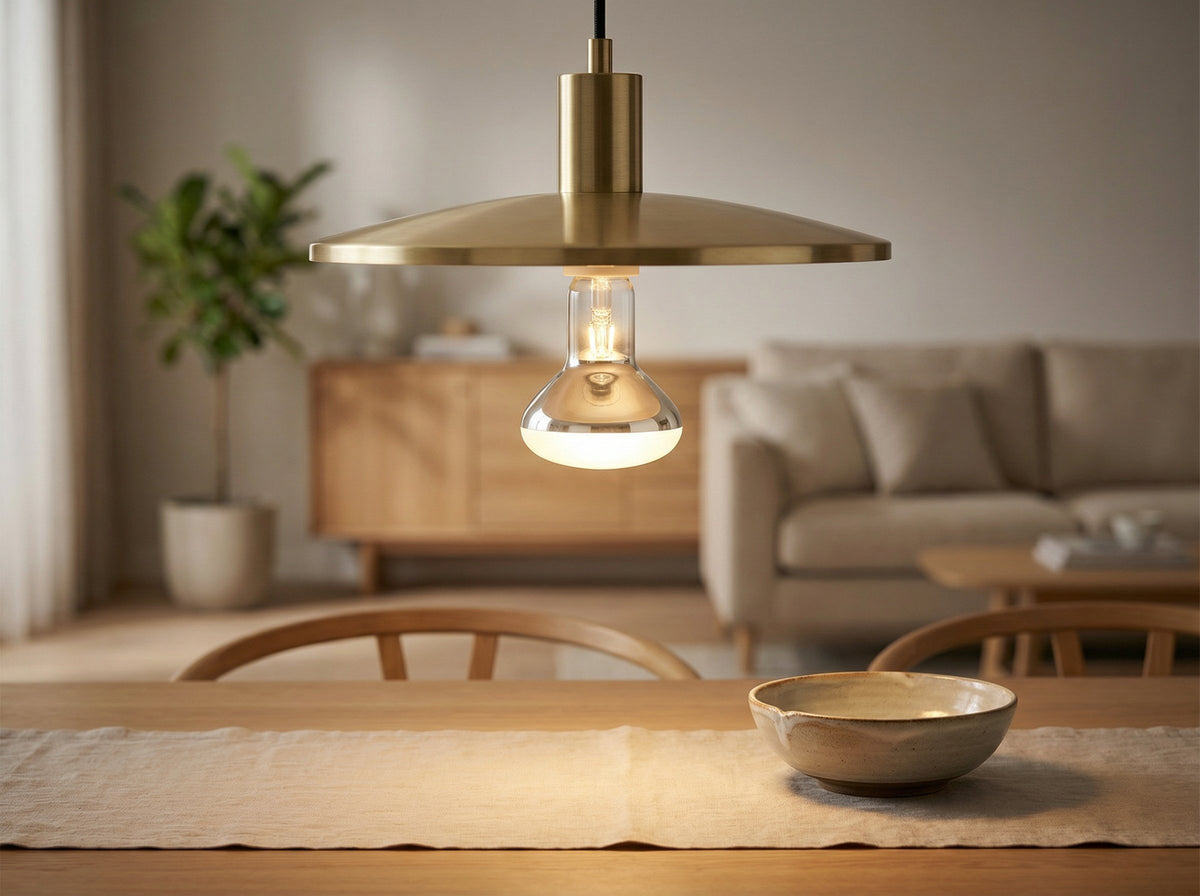 Ampoule réflecteur R63 E27 60W allumée sous une suspension en laiton, au-dessus d'une table en bois avec un bol