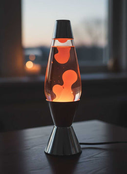 Lampe à lave à cire orange allumée sur une table en bois, devant une fenêtre au crépuscule
