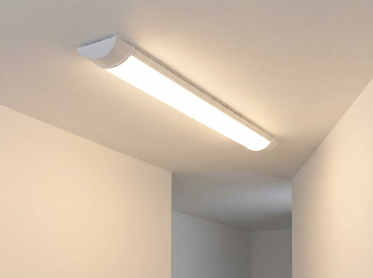 Réglette LED 60 cm allumée au plafond d'un couloir blanc, diffusant une lumière blanc chaud