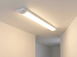 Réglette LED 60 cm allumée au plafond d'un couloir blanc, diffusant une lumière blanc chaud