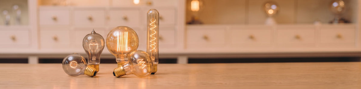 Ampoules vintage à filament apparent allumées, globes, poire et tube en verre ambré sur un comptoir en bois clair
