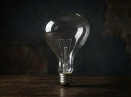 Ampoule R125 E27 en verre clair, filament visible, éteinte et posée sur un plateau en bois sombre